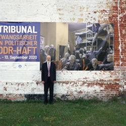 Thomas Schirrmacher vor dem Plakat des Tribunals an der Außenwand des ehemaligen Zuchthaus Cottbus © BQ/Martin Warnecke